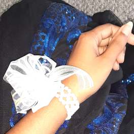 Hand wearing a white ribbon bracelet over black and blue sequined fabric