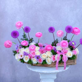 Pink and white flower arrangement in a wooden container with purple blooms