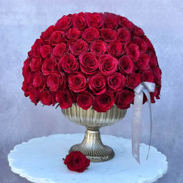 Red rose arrangement in a silver pedestal vase with a ribbon