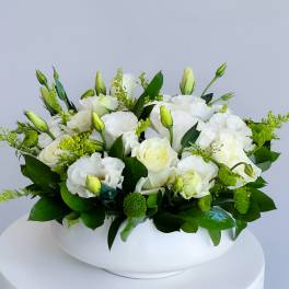 White floral arrangement in a low white vase with green accents