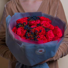 Bouquet of red roses with dark berry accents wrapped in blue paper