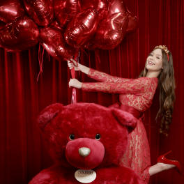Woman posing with red heart balloons and a giant red teddy bear