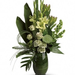 Tall green floral arrangement in a dark vase with lilies and tropical leaves