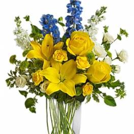 Yellow lilies and roses with blue delphinium in a clear vase