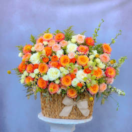 Basket arrangement of orange, pink, and white roses with a ribbon bow