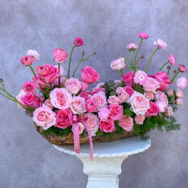 Pink roses and ranunculus arranged in a low basket on a pedestal