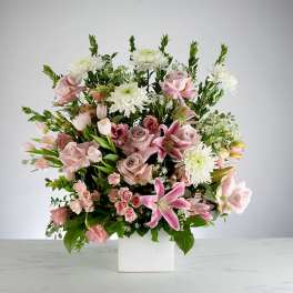 Tall arrangement of pink lilies, roses, and white mums in a white cube vase