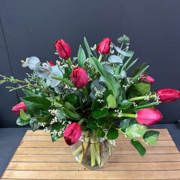 Pink tulips arranged in a clear glass vase with mixed greenery