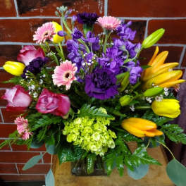 Mixed bouquet of pink, purple, and yellow flowers in a glass vase