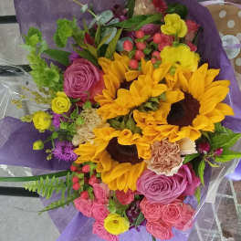 Bouquet with sunflowers, roses, and pink carnations wrapped in purple paper