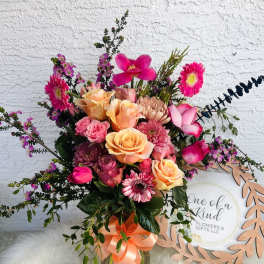 Mixed pink and peach flower bouquet in a glass vase with a ribbon