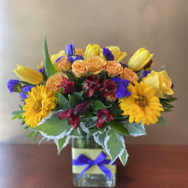 Mixed bouquet of yellow, orange, and purple flowers in a glass vase