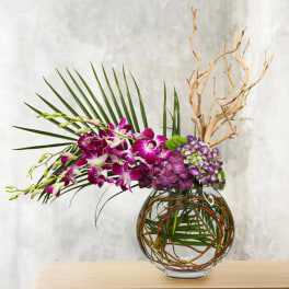 Purple orchids and hydrangeas in a glass vase with palm fronds and branches