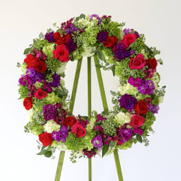 Large floral wreath on a stand with red, pink, purple, and green blooms