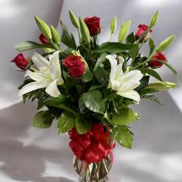 Red roses and white lilies arranged in a clear glass vase with a red ribbon.