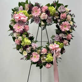 Heart-shaped floral wreath with pink flowers and a ribbon on a stand