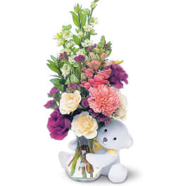 Bouquet of mixed flowers in a glass vase with a teddy bear