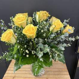 Yellow roses arranged in a clear glass vase with small white filler flowers