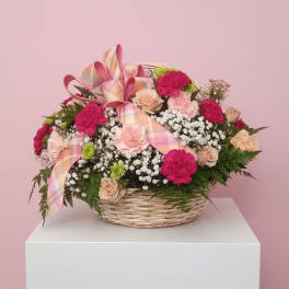 Basket arrangement of pink and peach flowers with a plaid ribbon