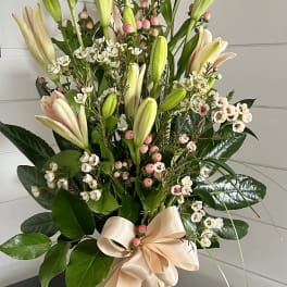 Tall bouquet of pale lilies and white filler flowers in a glass vase with a satin bow