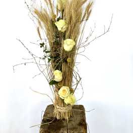 Tall arrangement of pale yellow roses with dried grasses on a wood base