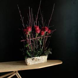Red roses arranged in a rectangular stone planter with tall twigs