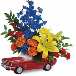 Bouquet of blue, yellow, orange, and red flowers in a red toy car container