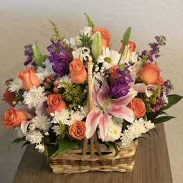 Basket arrangement of orange roses, pink lilies, and white daisies