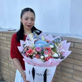 Woman holding a large pastel bouquet with lilies, roses, and blue hydrangeas