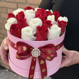 Red and white roses in a pink round box with a red ribbon