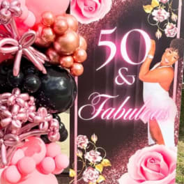 Pink and black balloon display beside a "50 & Fabulous" party sign