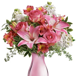 Pink roses and lilies arranged in a pink glass vase with white flowers