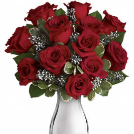 Red roses arranged in a clear glass vase with variegated greenery