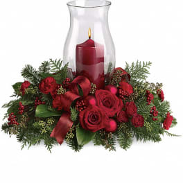 Red roses and greenery arranged around a glass hurricane candle holder