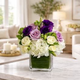 Purple, lavender, and white roses in a square glass vase