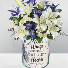 White lilies and blue irises in a glass vase with a memorial message