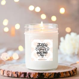 White scented candle in a glass jar with a "Follow your dreams" label