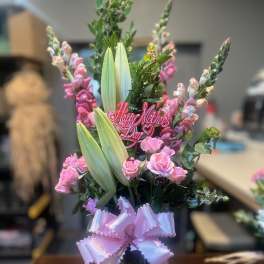 Pink roses and lilies in a glass vase with a pink ribbon and Mother's Day pick