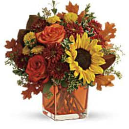 Autumn bouquet with sunflowers, roses, and fall leaves in a glass vase