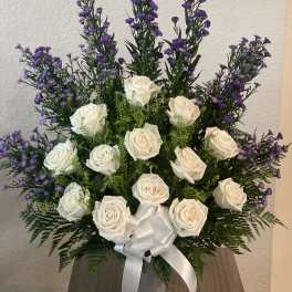 White roses and purple filler flowers in a white vase with a ribbon.