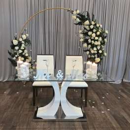 White rose arch over a glass table with candles and "Mr & Mrs" sign