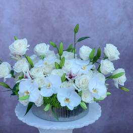 White roses and orchids arranged in a silver round container