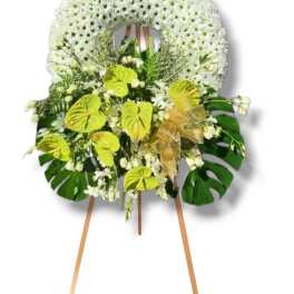 White floral standing wreath on an easel with green accents