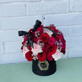 Red and pink rose arrangement in a black hat box with ribbon