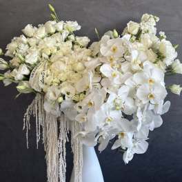 Large white floral arrangement in a tall vase with cascading orchids