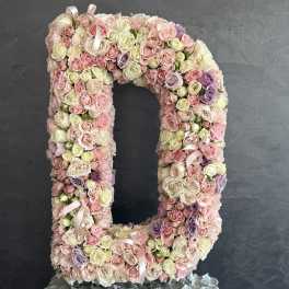 Large floral letter D covered in pastel roses and ribbons