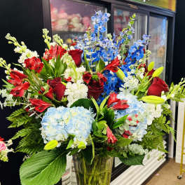 Mixed bouquet of red roses, blue delphinium, and pale hydrangeas in a glass vase