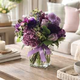 Purple bouquet in a clear glass vase with a lavender ribbon