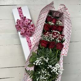 Bouquet of red roses in heart-patterned wrap beside a white gift box with pink ribbon