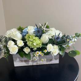 White roses and hydrangeas arranged in a wooden box with blue thistle accents.